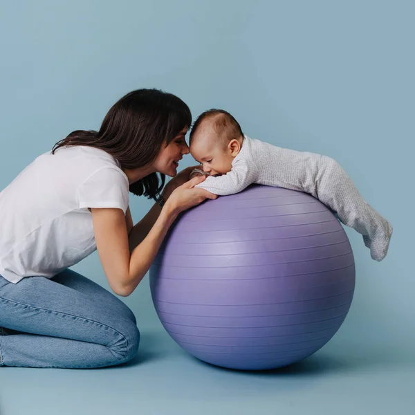 Šťastná matka dělá cvičení s dítětem dítěte na purpurovém míči jómu — Stock fotografie