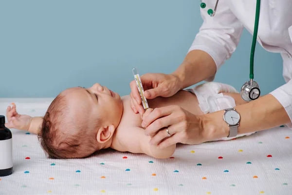 Doctor measuring temerature of a baby on a special table over blue background