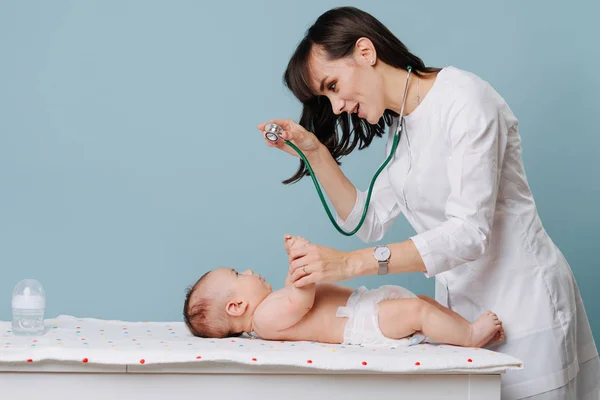 Médico examina bebê com estetoscópio em uma mesa especial sobre fundo azul — Fotografia de Stock