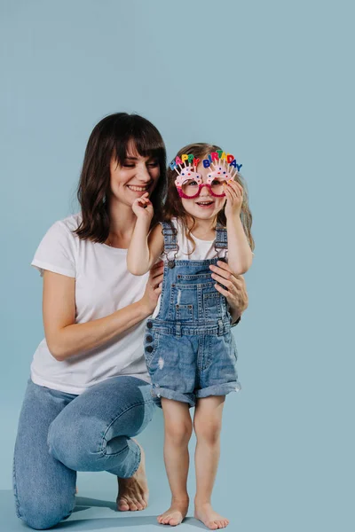 Anya és lánya boldog születésnapi szemüveggel játszik, mint a kék háttér — Stock Fotó