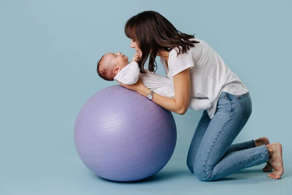 Gelukkige moeder doet oefeningen met haar baby kind op paarse yoga bal — Stockfoto