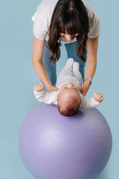 Happy mother doing exercises with her infant child baby on purple yoga ball — Stock Photo, Image