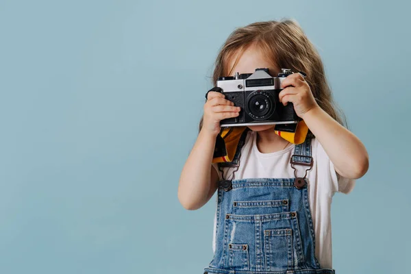 Little girl is taking an image with a vintage mirrored camera over blue. — Stock Photo, Image