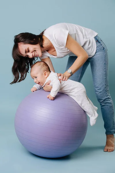 Gelukkige moeder doet oefeningen met haar baby kind op paarse yoga bal — Stockfoto
