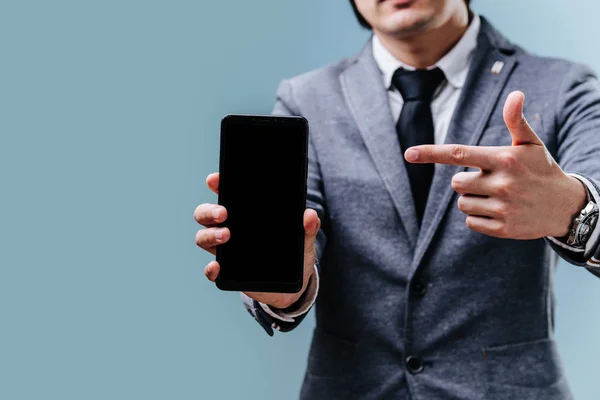 Zakenman wijst op zijn smartphone met wijsvinger over blauwe achtergrond — Stockfoto