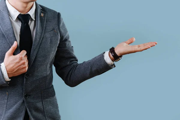 Empresario con traje apuntando a algo con una mano abierta sobre fondo azul — Foto de Stock