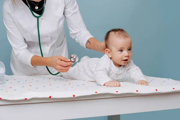 Doctor exams baby with stethoscope on a special table over blue background