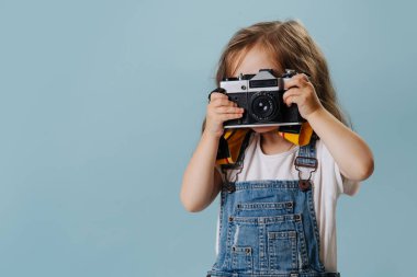 Küçük kız mavi üzerinde bir vintage aynalı kamera ile bir görüntü alıyor.