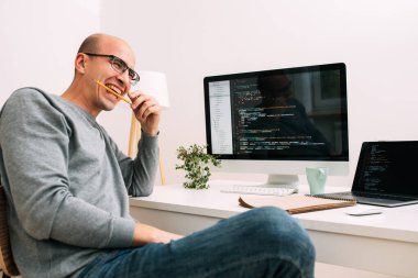 Programcı, kod satırlarıyla dolu iki ekranla masanın arkasında çalışıyor.