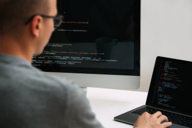 Programcı, masanın arkasında çalışıyor, siyah ekrandaki kodu analiz ediyor..