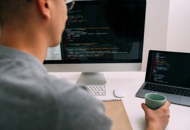 Programcı, masanın arkasında çalışıyor, siyah ekrandaki kodu analiz ediyor..