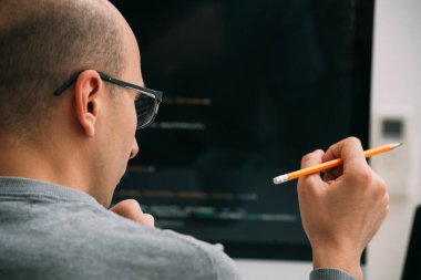 Programcı, masanın arkasında çalışıyor, siyah ekrandaki kodu analiz ediyor..
