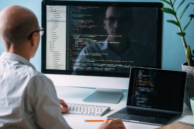Programcı, masanın arkasında çalışıyor, siyah ekrandaki kodu analiz ediyor..
