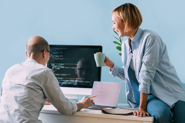 Programador, trabajando detrás del escritorio, analizando código mientras chatea con su compañero de trabajo —  Fotos de Stock