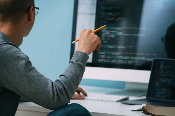 Programador, trabajando detrás del escritorio, analizando código en la pantalla negra . — Foto de Stock