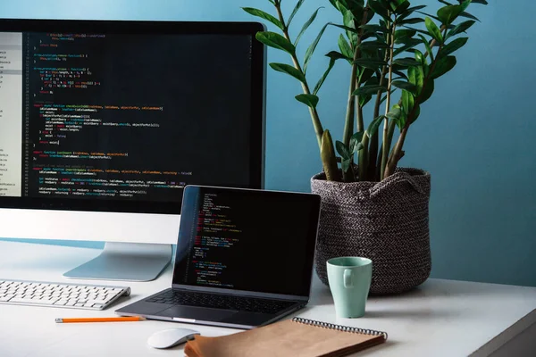 Two black screens, laptop and monitor, filled with program code lines on desk.