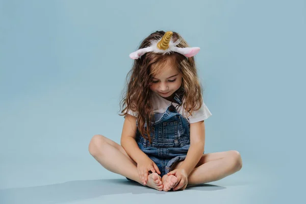 Menina criança sentada de pernas cruzadas usando headband com chifre de unicórnio e orelhas — Fotografia de Stock