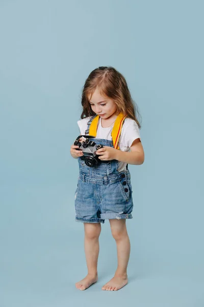 Little girl in denim overall looking at retro camera