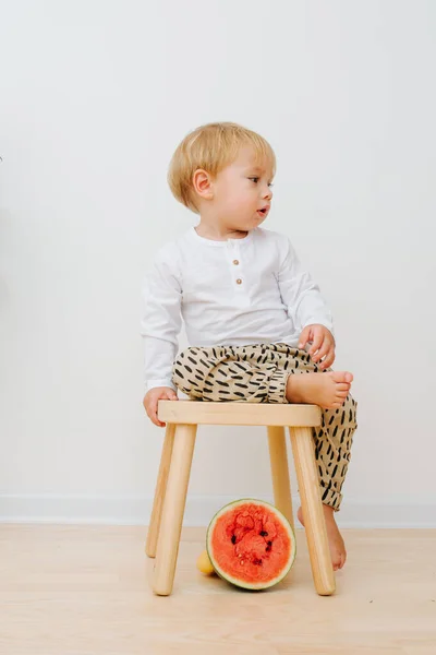 Little toddler boy sitting on stool. Red watermelon half slice is under it. — Stock Photo, Image