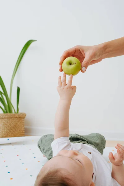 Дитина лежить на спині і тягнеться до яблука. — стокове фото