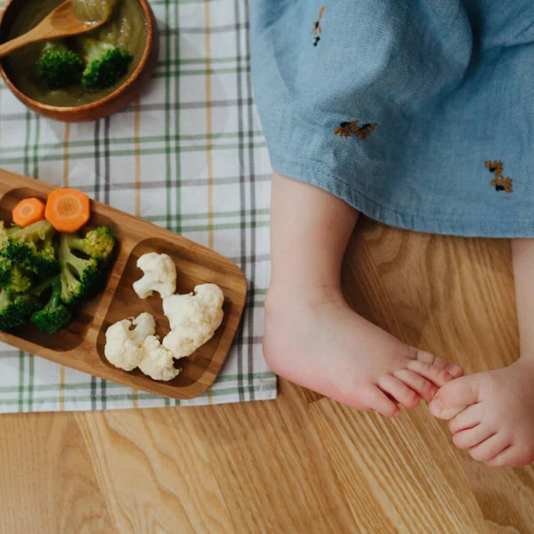 Ноги маленька дівчинка і тарілка з овочами — стокове фото