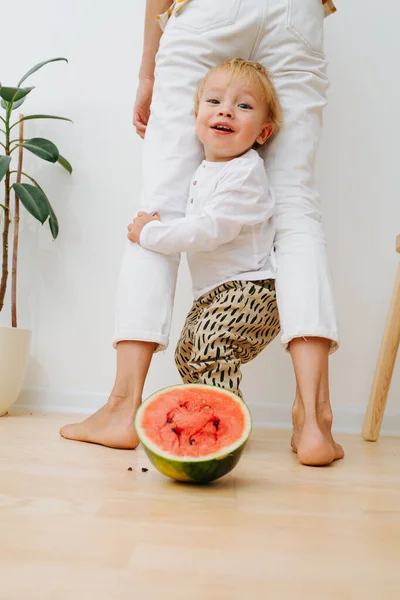 Little toddler boy, mother's legs arch and watermelon half slice — Stock Photo, Image