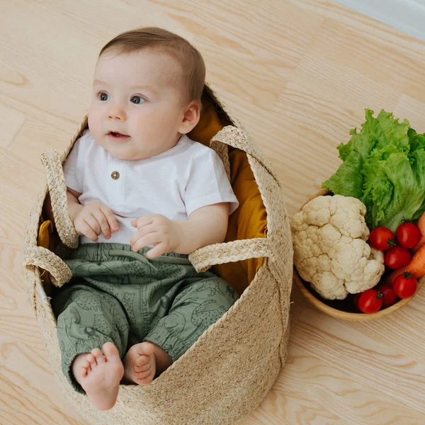 Infant baby in a woolven like bag and bowl of vegetables nearby — Stock Photo, Image