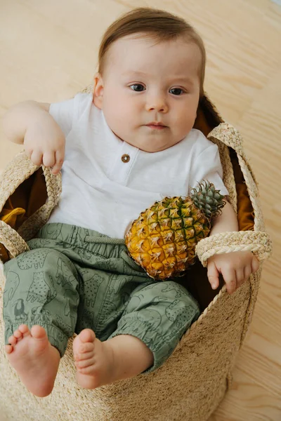 Infant baby with pineapple in a wicker, basket like bag — Stock Photo, Image