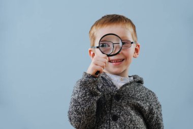 Gözlüklü şirin kızıl çocuk büyüteçten mavi gözlüklere bakıyor.