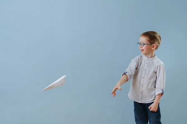 Cute little ginger boy launched a paper plane to fly over blue background — Stockfoto