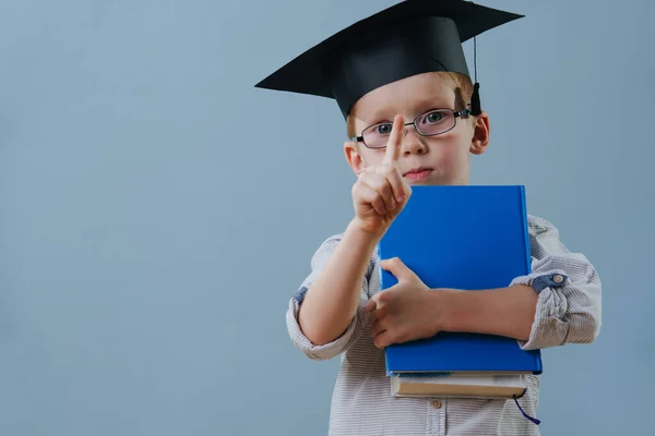 Redhead first grader boy in glasses and student hat with pointing finger up