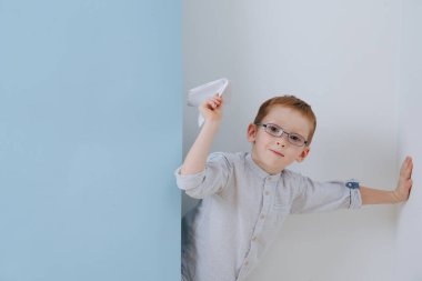 Küçük tatlı kızıl çocuk, köşeden kağıt bir uçak fırlatmak üzere.