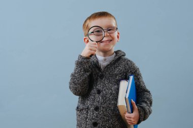 Gözlüklü komik kızıl çocuk büyüteçten mavi gözlüklere bakıyor.