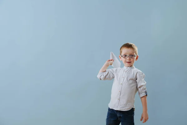 Cute little ginger boy, about to launch a paper plane over blue background — Stockfoto