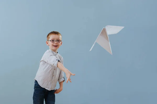 Cute little ginger boy launched a paper plane to fly over blue background — Stockfoto