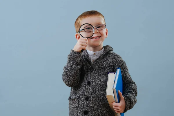 Divertido pequeño jengibre en gafas mirando a través de lupa sobre azul — Foto de Stock