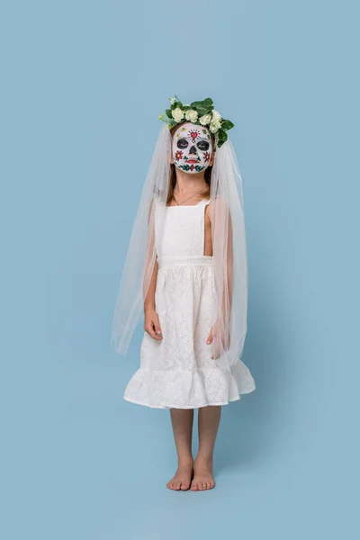 Petite fille en robe de mariée porte peint masque de crâne effrayant sur fond bleu — Photo