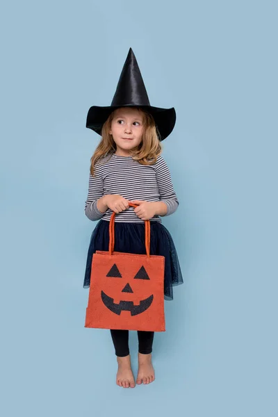 Portrait of a little girl in witch hat and black clothing holding halloween bag — Stock Photo, Image