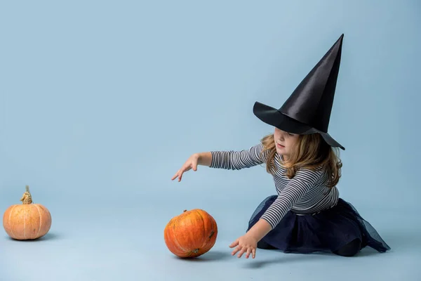 Bambina in cappello da strega e vestiti neri con giocare con la zucca sopra il blu — Foto Stock