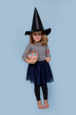 Cadılar Bayramı 'nda cadı kostümü giymiş sinsi bir kız şeker ve lolipop tutuyor.