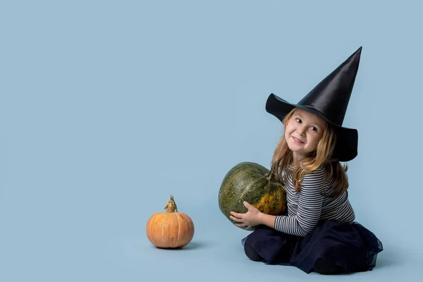 Malá čarodějka si hraje s dýněmi sedícími na podlaze — Stock fotografie