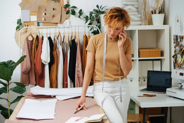 A young woman in a tailoring studio, talking to clients on the phone