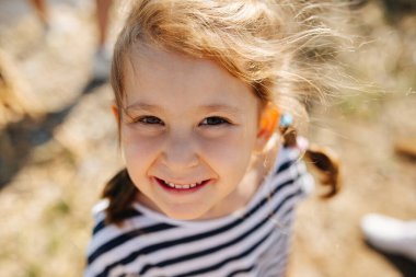 Güneşli bir günde neşe dolu küçük bir anaokulu kızının aşağı açılı portresi. Bulanık kuru çimen arkaplanı.