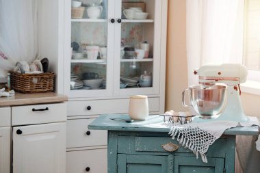 Dolabı sıkışık küçük bir mutfak. Ortasında pasta pişirmek için yumurta ve mikser olan eski masa..