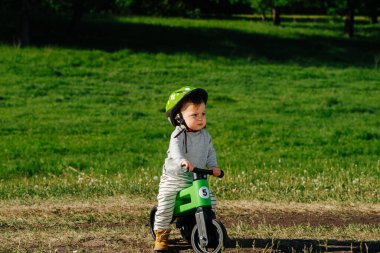 Huysuz küçük çocuk kırsalda üç tekerli bisiklete biniyor. Koruyucu kask takıyor. Çimlerin üzerinde.