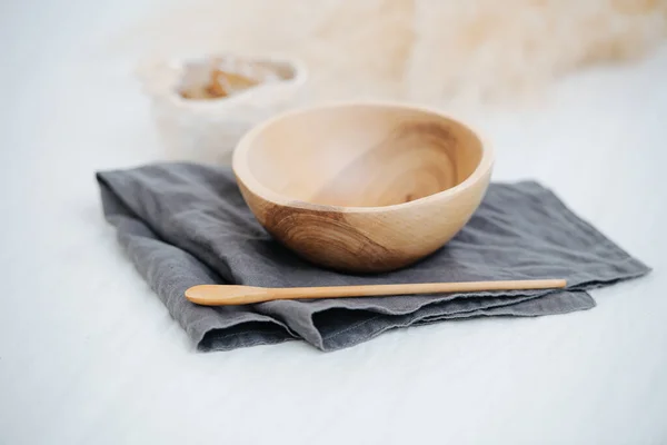 Image of a handmade wooden bowl, smoothed and varnished, standing on a napkin on a white surface. Wooden spoon and oatmeal bowl complete this composition.