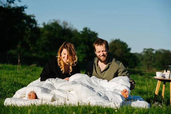 Sonriente pareja aturdida despertando de una siesta en la cama hecha afuera en un campo — Foto de Stock