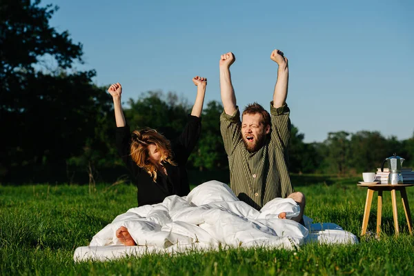 Pareja soñolienta estirándose en la cama hecha al aire libre en un campo, despertando —  Fotos de Stock