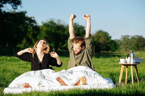 Couple resting on bed made outside on a grass in a countryside, waking up — Stock Photo, Image