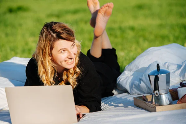 Distracted woman looks at someone while working on laptop, lying in bed outdoors